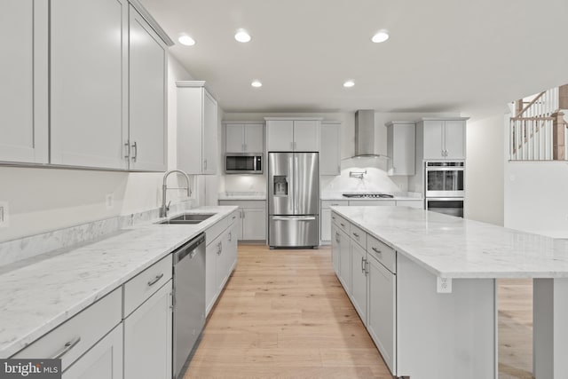 kitchen with a kitchen island, sink, light hardwood / wood-style floors, stainless steel appliances, and wall chimney range hood