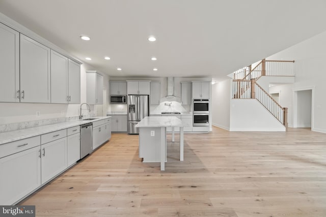 kitchen with sink, a center island, stainless steel appliances, wall chimney range hood, and light wood-type flooring