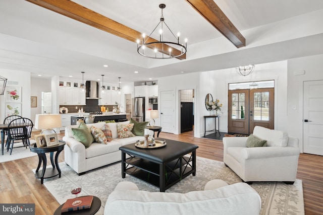 living room featuring a notable chandelier, beam ceiling, light hardwood / wood-style flooring, and french doors