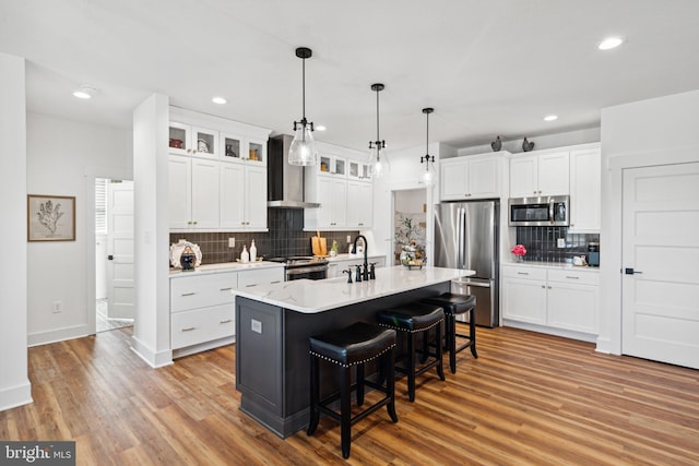 kitchen with a kitchen island with sink, white cabinetry, stainless steel appliances, and light wood-type flooring