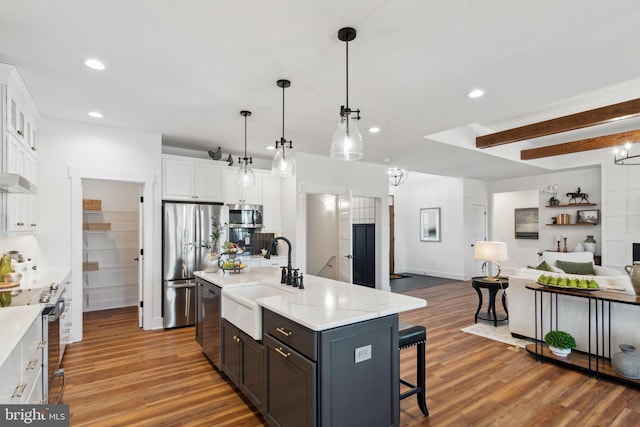 kitchen featuring sink, white cabinetry, decorative light fixtures, stainless steel appliances, and a kitchen island with sink