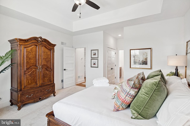 bedroom with connected bathroom, ceiling fan, a tray ceiling, light carpet, and a closet