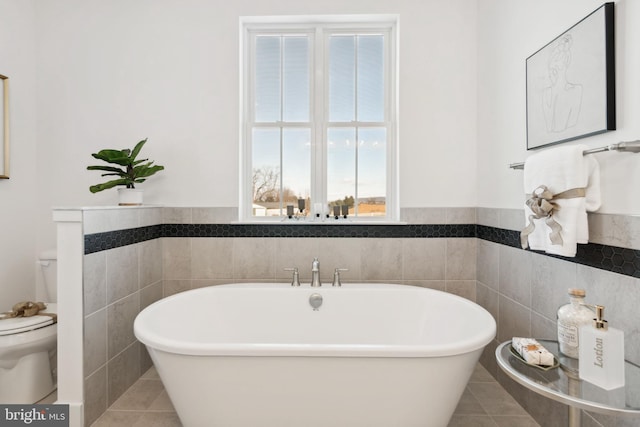 bathroom with a washtub, tile patterned flooring, tile walls, and toilet