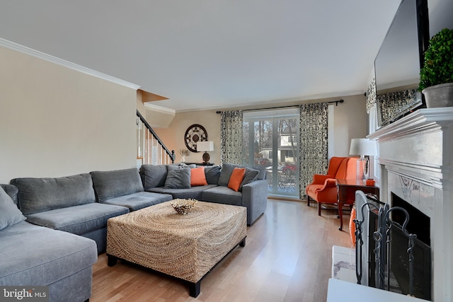 living room featuring crown molding, a tiled fireplace, and light hardwood / wood-style flooring