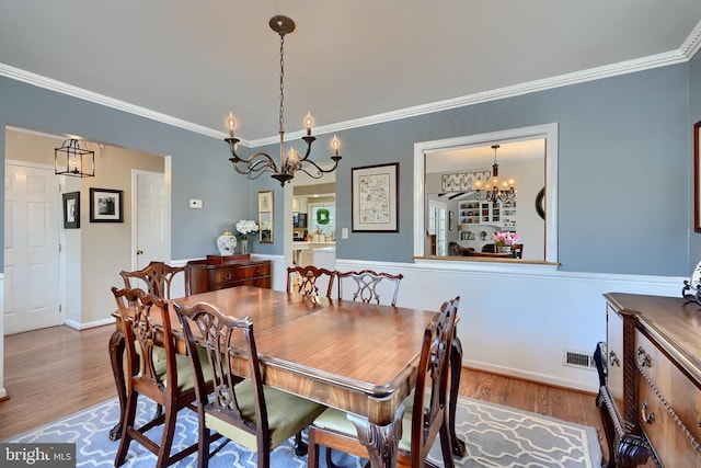 dining room with hardwood / wood-style flooring, crown molding, and a notable chandelier