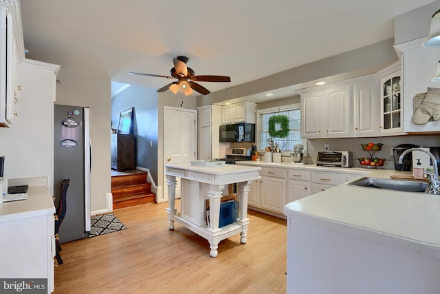 kitchen with stainless steel appliances, sink, white cabinets, and light hardwood / wood-style flooring