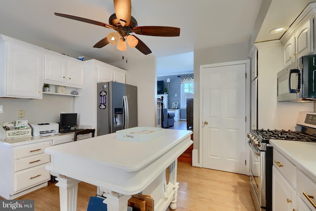 kitchen with appliances with stainless steel finishes, built in desk, white cabinets, and light hardwood / wood-style floors