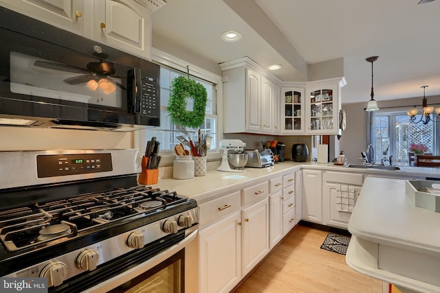 kitchen featuring sink, white cabinets, hanging light fixtures, gas stove, and light hardwood / wood-style flooring