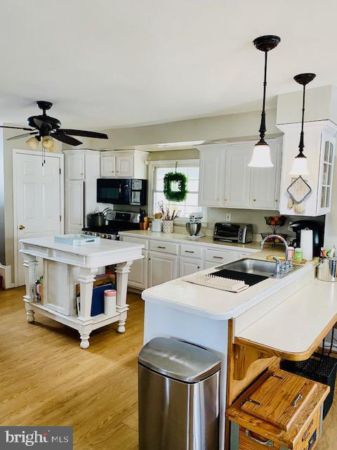 kitchen featuring pendant lighting, white cabinets, a kitchen bar, range, and light wood-type flooring