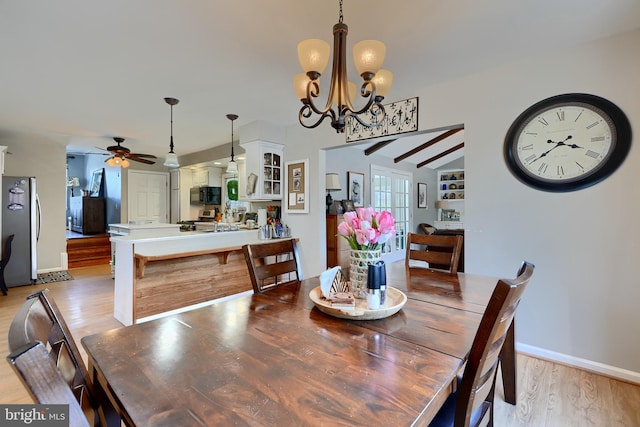 dining area featuring vaulted ceiling with beams, ceiling fan with notable chandelier, and light hardwood / wood-style flooring