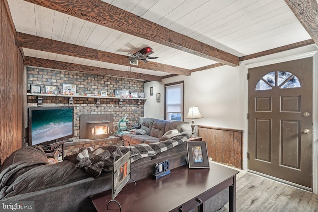 living room featuring a fireplace, beam ceiling, wooden walls, and light hardwood / wood-style floors