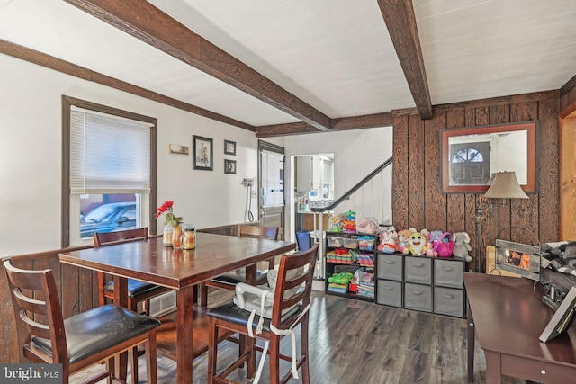 dining area featuring beam ceiling, dark wood-type flooring, and wooden walls