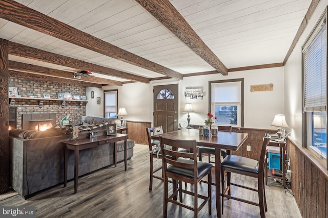 dining space with hardwood / wood-style flooring, a fireplace, beam ceiling, and wood walls