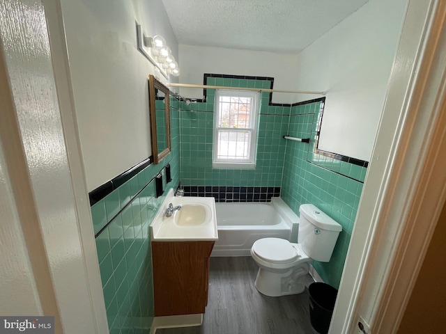 full bath with a textured ceiling, toilet, a wainscoted wall, wood finished floors, and tile walls