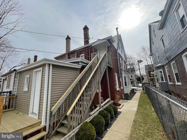 view of side of home featuring stairs, a chimney, and fence