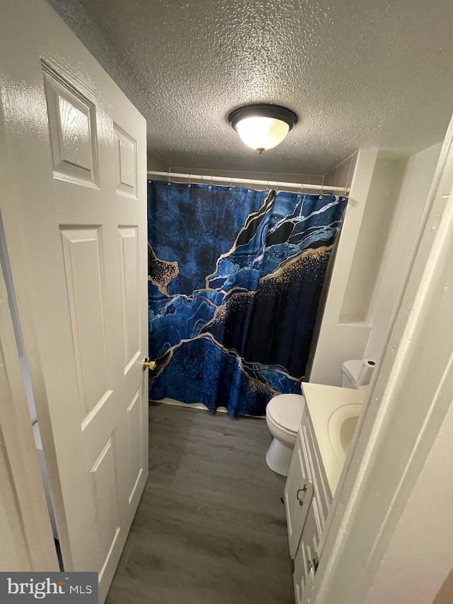 full bath with toilet, vanity, a textured ceiling, and wood finished floors