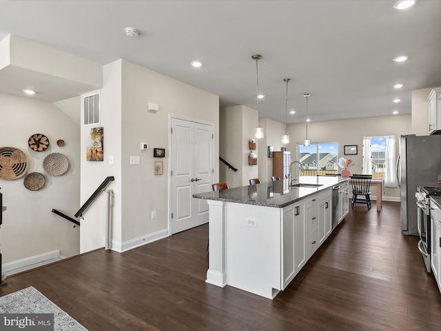 kitchen with decorative light fixtures, white cabinetry, dark stone countertops, dark hardwood / wood-style flooring, and a center island with sink