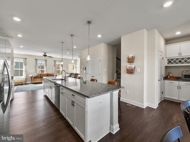 kitchen featuring sink, a center island with sink, appliances with stainless steel finishes, light stone countertops, and white cabinets