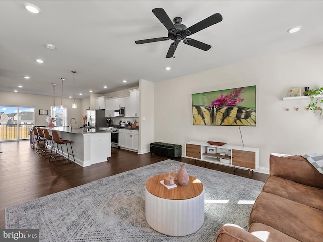 living room with dark wood-type flooring, ceiling fan, and sink