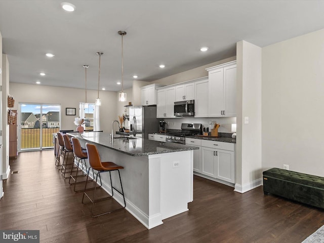 kitchen with appliances with stainless steel finishes, an island with sink, hanging light fixtures, and white cabinets