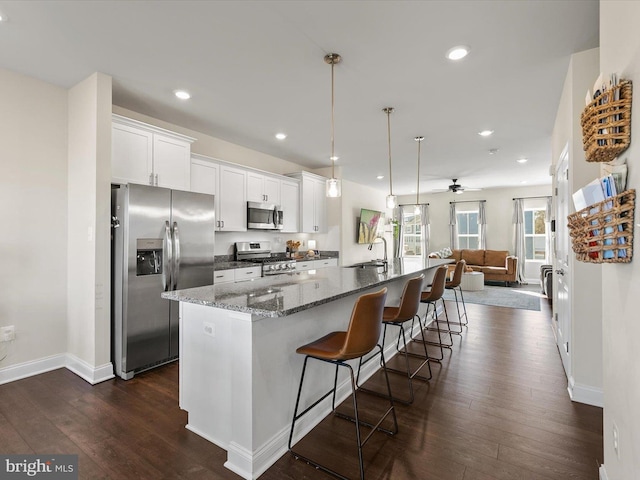 kitchen featuring appliances with stainless steel finishes, decorative light fixtures, white cabinetry, a kitchen bar, and a large island with sink