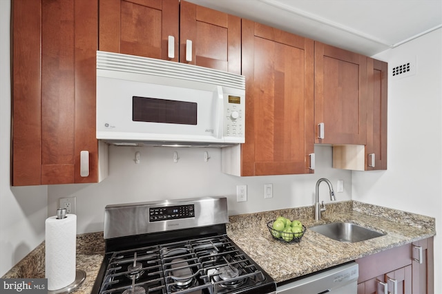 kitchen featuring white appliances, sink, and stone counters