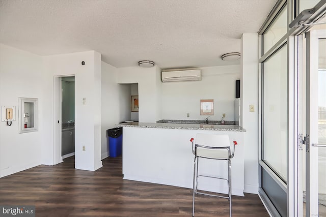 kitchen featuring dark wood-type flooring, light stone counters, a textured ceiling, kitchen peninsula, and a wall unit AC