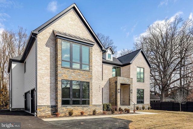 view of front facade with aphalt driveway, stone siding, brick siding, and fence