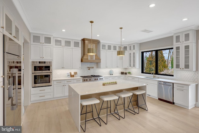 kitchen with glass insert cabinets, light countertops, premium range hood, and appliances with stainless steel finishes