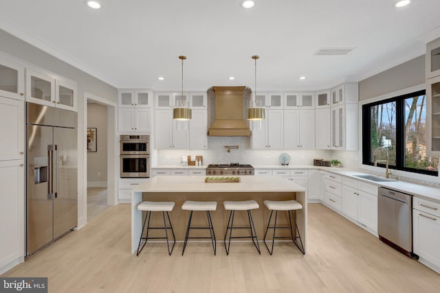 kitchen with a center island, custom range hood, appliances with stainless steel finishes, glass insert cabinets, and a sink