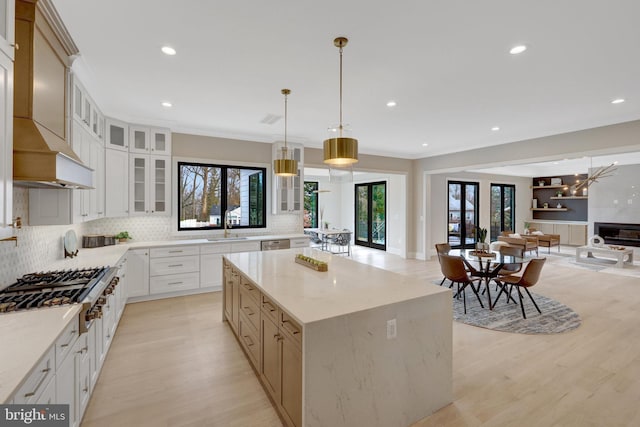 kitchen featuring a spacious island, glass insert cabinets, open floor plan, decorative light fixtures, and white cabinetry