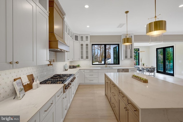 kitchen featuring glass insert cabinets, a center island, light stone countertops, white cabinetry, and pendant lighting