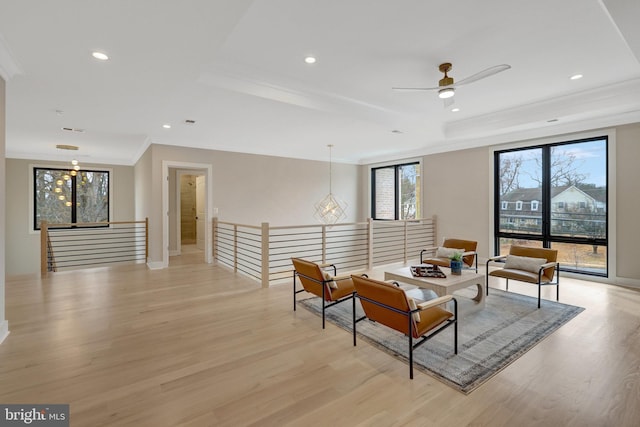 living area with ornamental molding, a tray ceiling, light wood-style flooring, and an upstairs landing