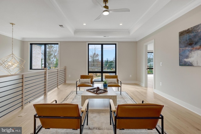 living area featuring ornamental molding, a tray ceiling, light wood-type flooring, and visible vents