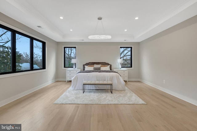 bedroom with light wood-style flooring, multiple windows, and a tray ceiling