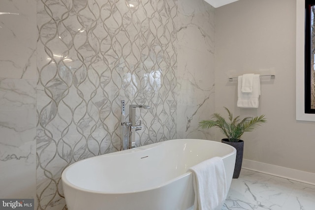 bathroom with marble finish floor, a freestanding bath, and baseboards