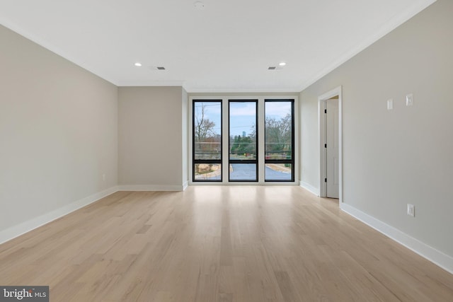 empty room featuring light wood-style floors, visible vents, baseboards, and ornamental molding