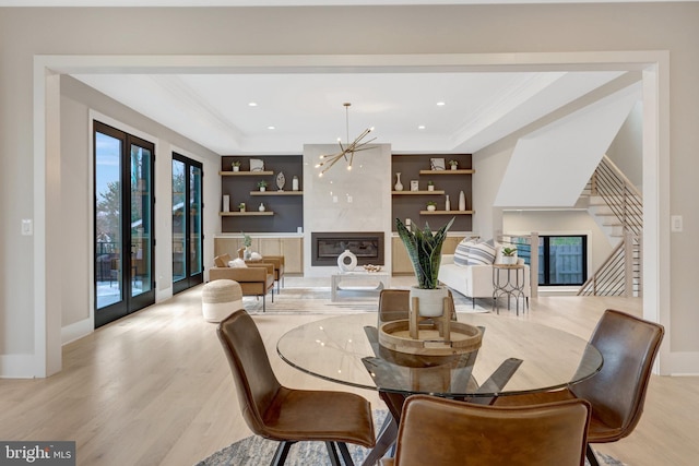 dining room with light wood-style flooring, a premium fireplace, stairway, ornamental molding, and a tray ceiling