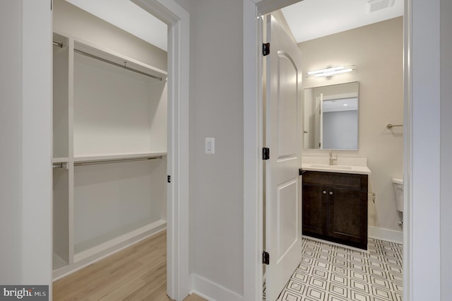 half bathroom with toilet, visible vents, vanity, baseboards, and a walk in closet