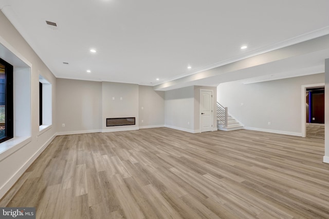 unfurnished living room with baseboards, stairway, a glass covered fireplace, and light wood-style floors