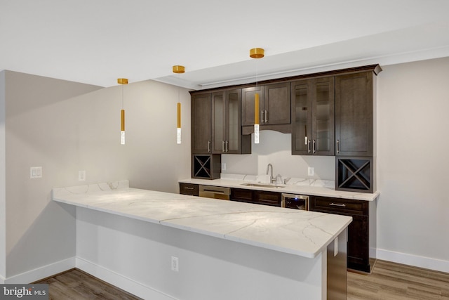 kitchen with a peninsula, a sink, light wood-style flooring, and pendant lighting