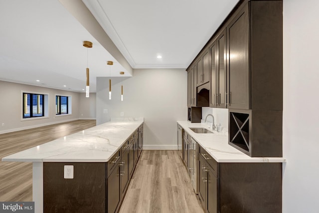 kitchen with dark brown cabinets, a sink, decorative light fixtures, and light stone countertops