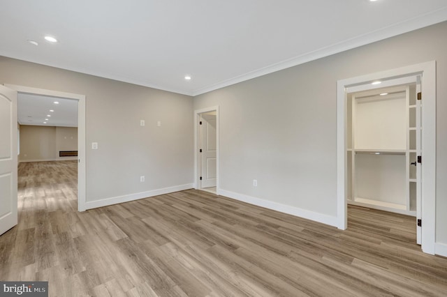 unfurnished bedroom featuring light wood-style floors, a spacious closet, baseboards, and ornamental molding