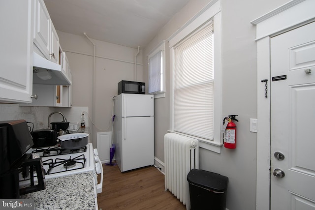 kitchen with radiator, white appliances, tasteful backsplash, wood-type flooring, and white cabinets