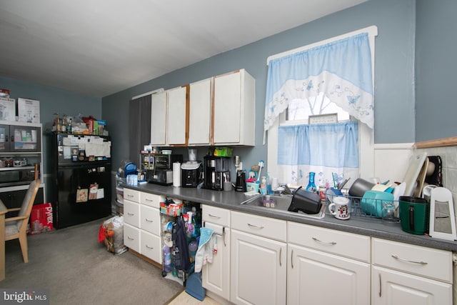 kitchen featuring white cabinetry, sink, and black fridge