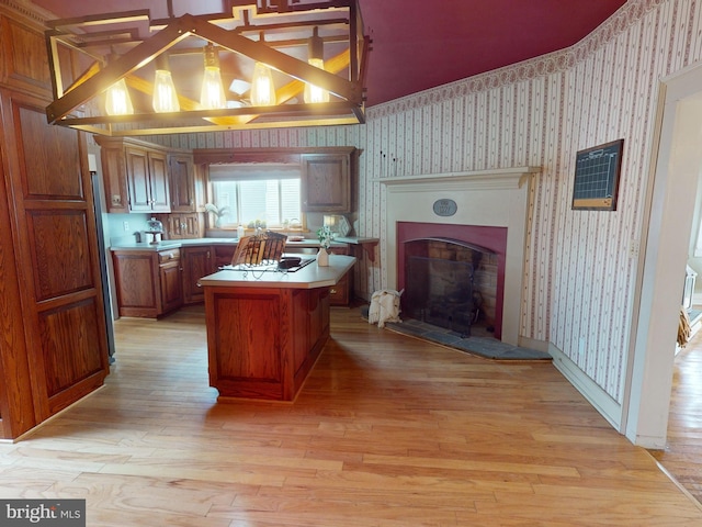 kitchen featuring a center island, light countertops, brown cabinetry, light wood-type flooring, and wallpapered walls