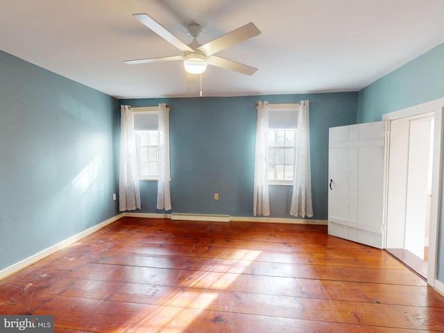 unfurnished bedroom with a ceiling fan, a baseboard radiator, baseboards, and hardwood / wood-style floors