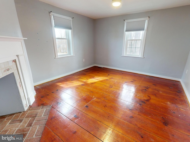 unfurnished living room with wood-type flooring, a wealth of natural light, and baseboards