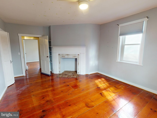 unfurnished living room featuring wood-type flooring, baseboards, and a tile fireplace