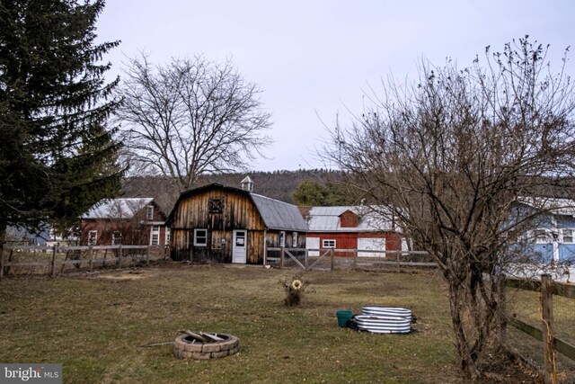 back of house featuring a barn, an outdoor fire pit, a gambrel roof, an outbuilding, and fence